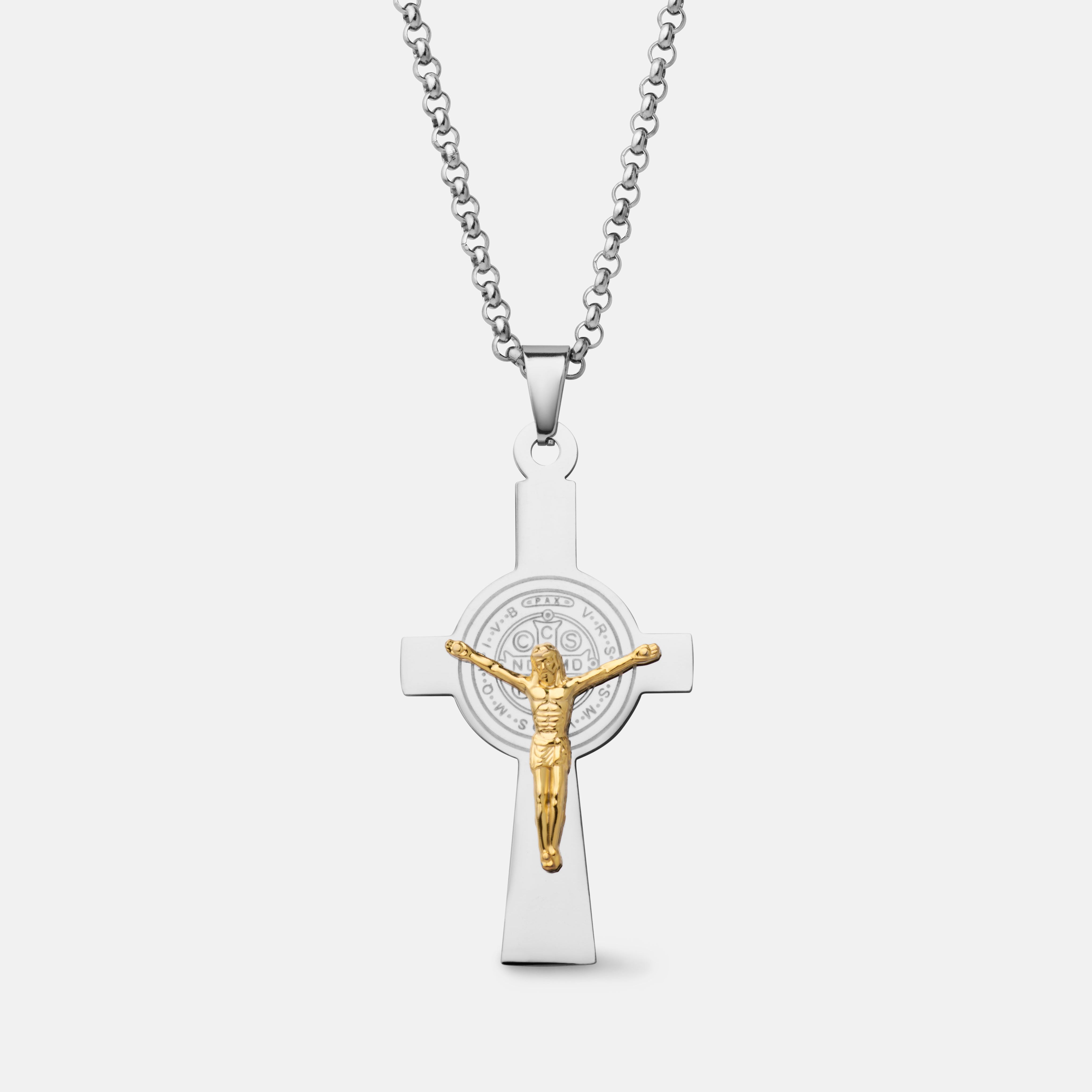 A silver cross pendant necklace featuring a gold-toned crucifix and a circular Saint Benedict emblem in the center, suspended from a silver box chain against a light gray background.